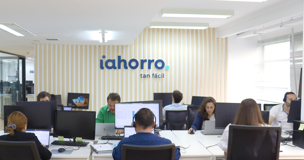 Varios trabajadores en sus puestos de trabajo, al fondo, el logo de iAhorro en una pared.